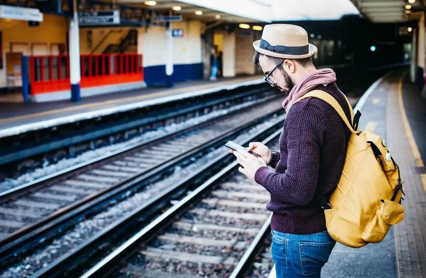 Foto de Clem Onojeghuo de hombre texteando en su celular junto a unas vías de tren
